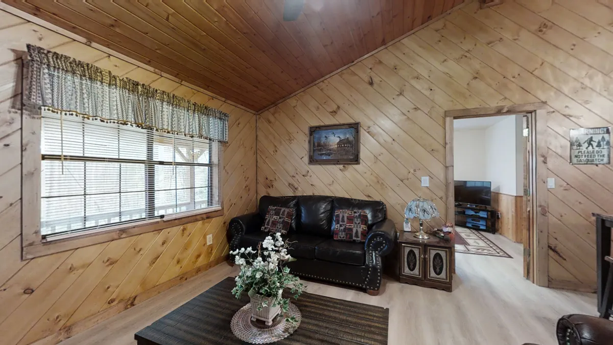 A comfortable leather sofa facing a coffee table with fresh flowers, set against a backdrop of large windows and wall art. The scene radiates warmth and invites guests to unwind, socialize, or enjoy a quiet moment with friends.