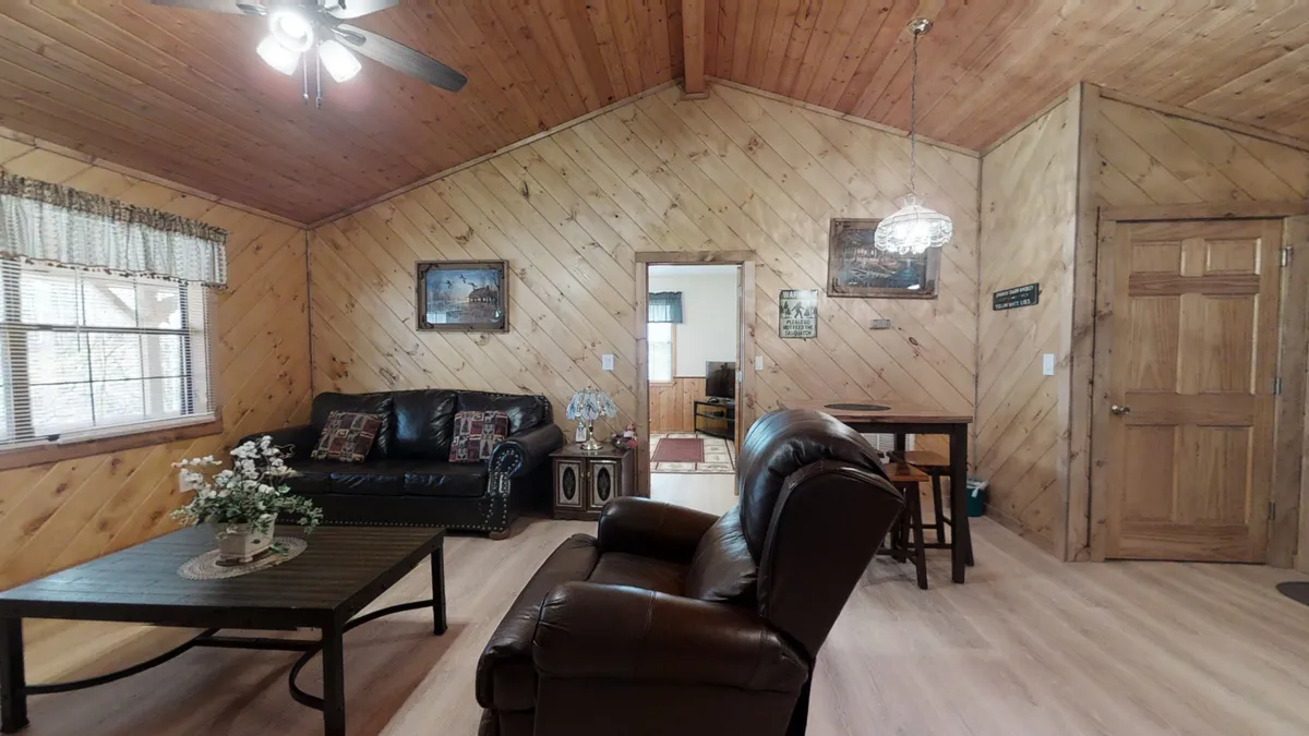A cozy living area with a leather sofa, wooden coffee table, decorative flowers, and pictures adorning the wall. The warm lighting and arrangement encourage intimate gatherings, whether for game nights or quiet evenings with loved ones.