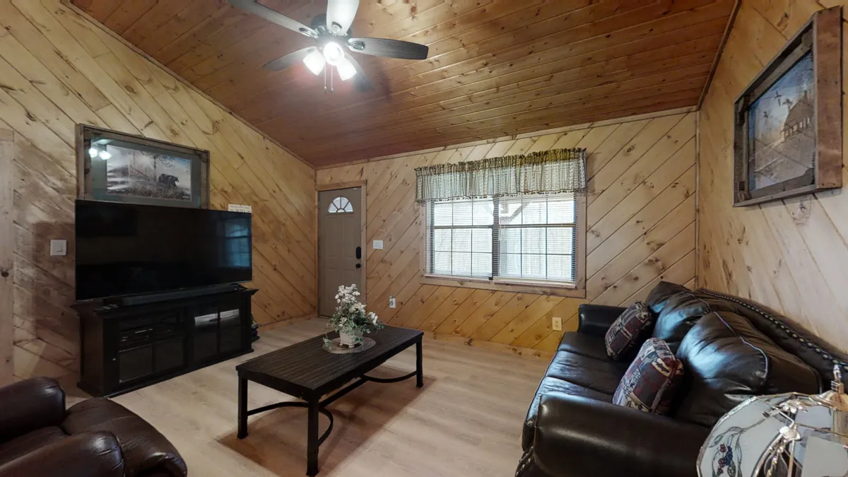 A warm living space featuring a leather sofa, coffee table, television, wooden walls, and a window with curtains. The scene feels intimate yet inviting, perfect for relaxing, watching TV, reading, or gathering with friends and family after a day of adventure.