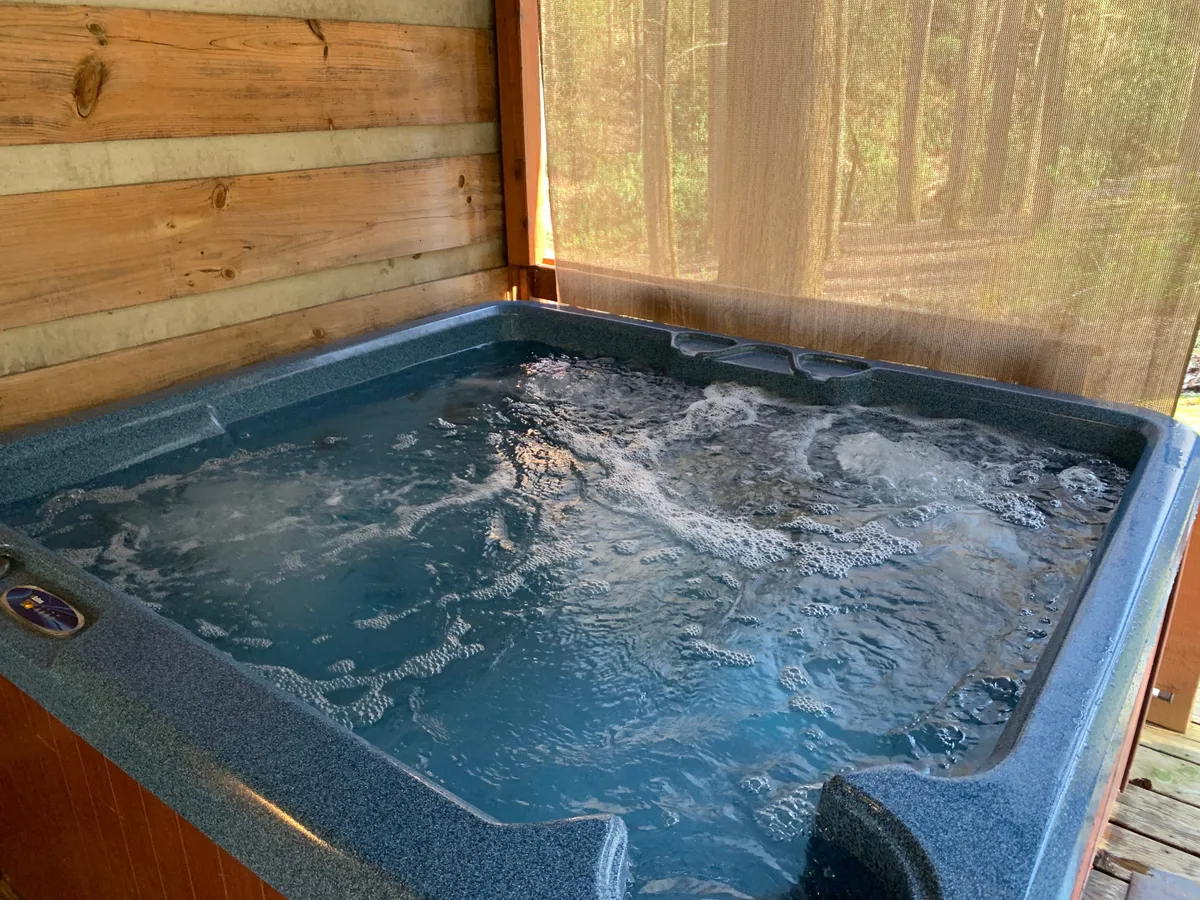 This image features a tranquil hot tub nestled within a screened enclosure framed by rustic wooden walls. The space opens up to the natural surroundings, allowing for stargazing or listening to the gentle sounds of the forest while soaking. Soft lighting and comfortable seating invite relaxation, making it an ideal spot for unwinding after a day outdoors.