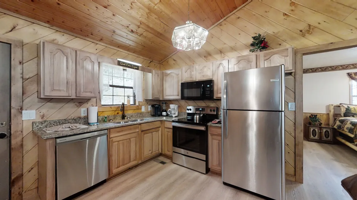 This image spotlights a warm, inviting kitchen area complete with granite countertops, stainless steel appliances, and wooden cabinets. A chandelier overhead adds a homey touch, suggesting a space ideal for both meal prep and social gatherings.
