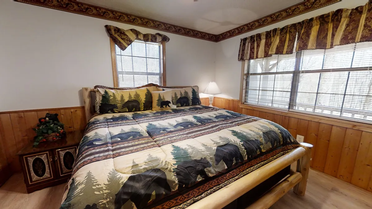 A warmly lit bedroom with a bear-themed bedspread, rustic wooden furniture, and large windows letting in soft natural light. The space exudes a cozy mountain ambiance ideal for unwinding after outdoor adventures.