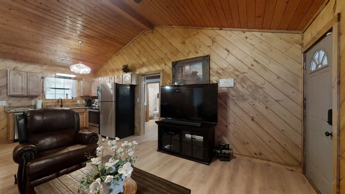 A cozy communal living area featuring a leather armchair and sofa, a television, a well-equipped kitchen in the background, and a coffee table adorned with decorative flowers. The space is warm and welcoming, inviting guests to gather, share meals, and relax together after a day of adventure.
