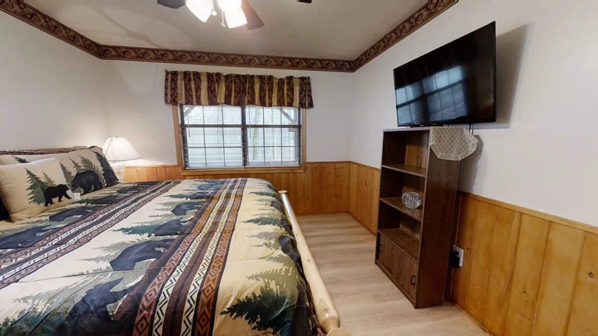 A comfortable king bedroom with patterned bedding, wooden furnishings, and a TV mounted on the wall. The room invites relaxation for movie nights or quiet mornings, blending functionality with comfort.